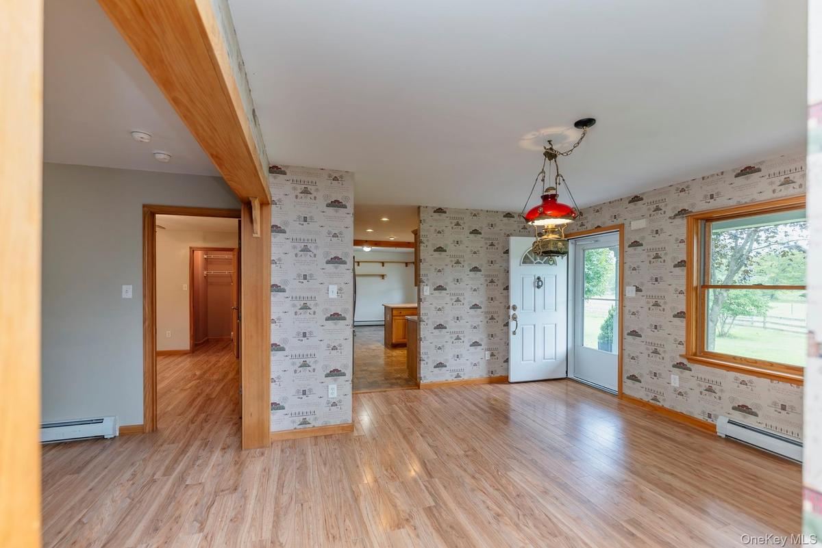 Foyer entrance featuring a baseboard radiator, wallpapered walls, baseboards, and light wood-type flooring
