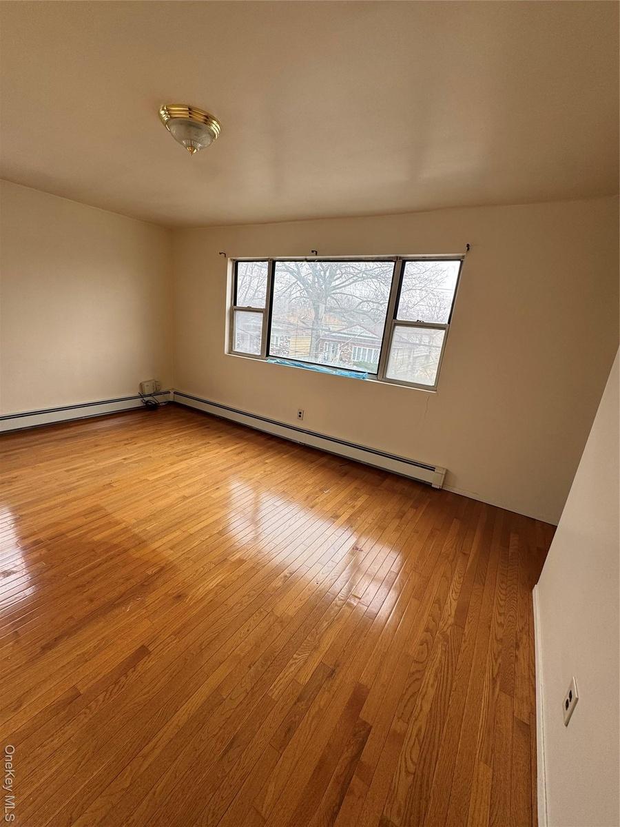 Empty room featuring hardwood / wood-style floors and a baseboard radiator