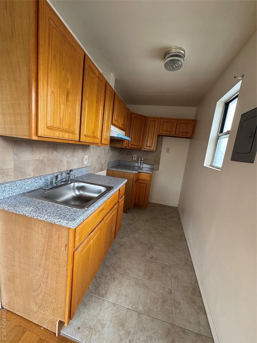 Kitchen featuring a sink, brown cabinets, decorative backsplash, electric panel, and range hood