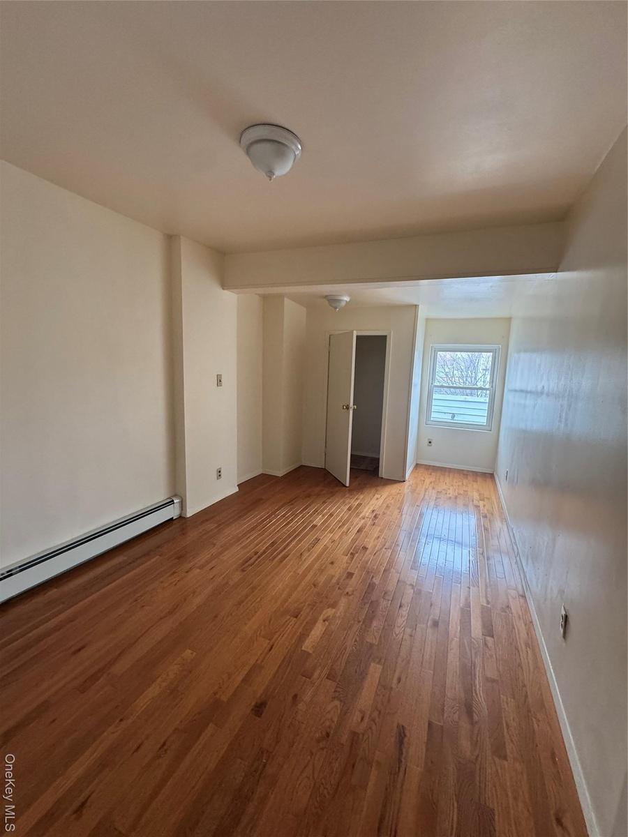 Spare room with baseboards, wood finished floors, and a baseboard radiator