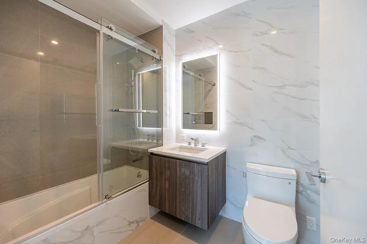 Full bath with vanity, tile walls, toilet, and shower / bath combination with glass door