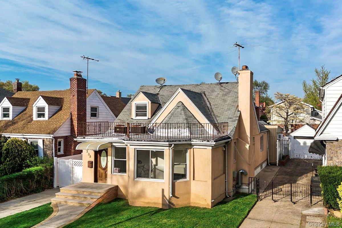 Front view of house with a chimney, fence, a balcony, and stucco siding