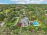An aerial side perspective reveals the property’s architectural elegance, featuring a sunroom framed by floor-to-ceiling windows, and lushly landscape