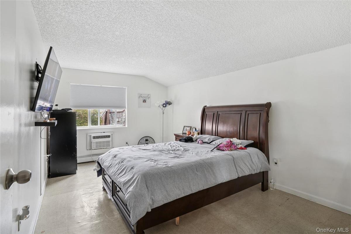 Bedroom with a baseboard heating unit, a textured ceiling, lofted ceiling, tile patterned floors, and an AC wall unit