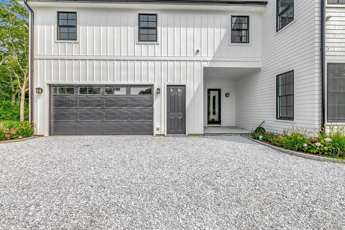 Modern inspired farmhouse with board and batten siding, gravel driveway, covered porch, and an attached garage