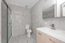 Bathroom featuring wall-to-wall stone-finish tile, a wood-finish vanity with an integrated basin, a polished chrome single-handle faucet, a glass-encl