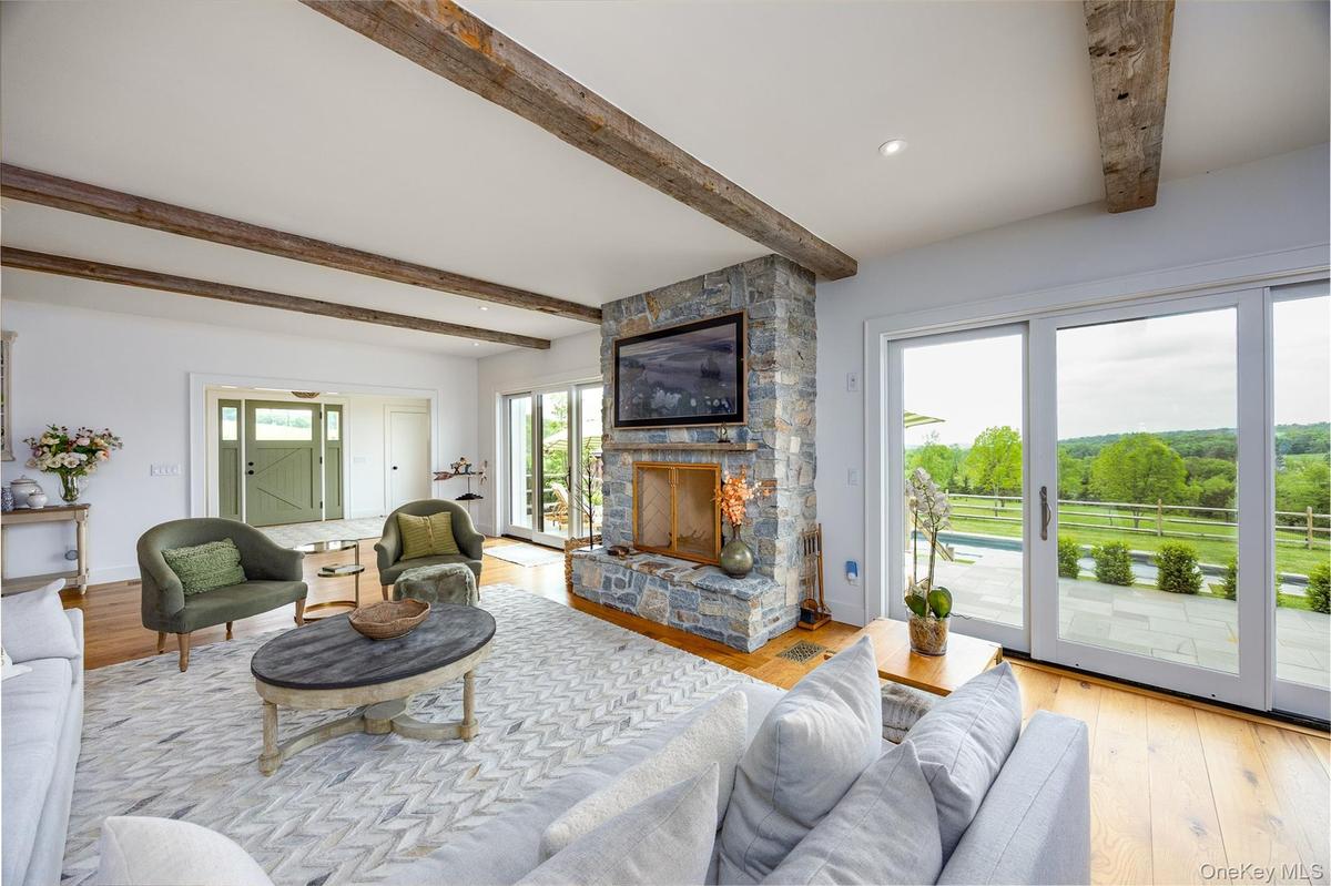 Living room with beamed ceiling, a stone fireplace, wood finished floors, and recessed lighting