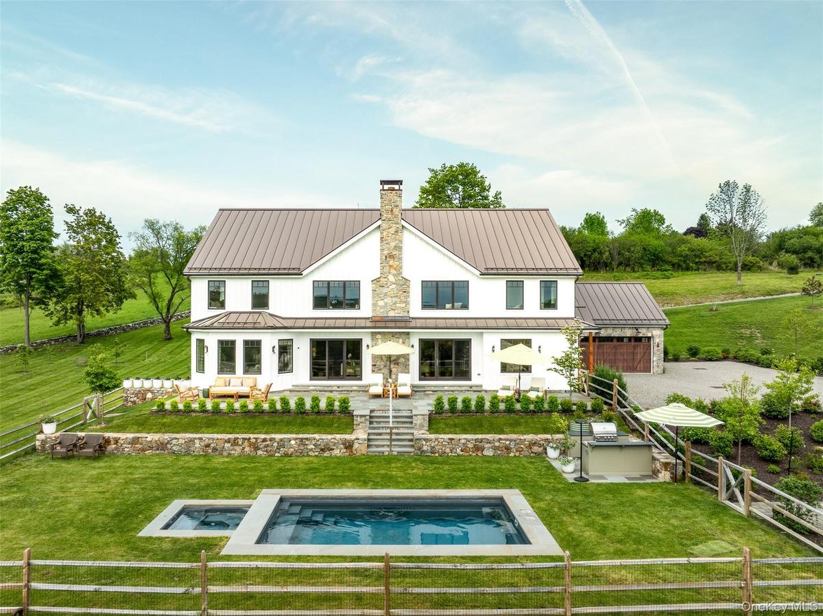 Back of house featuring a chimney, a standing seam roof, an outdoor pool, an in-ground hot tub, and an attached garage