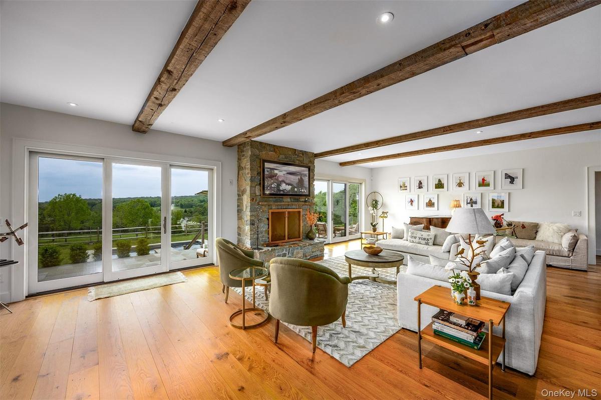 Living area with hardwood / wood-style floors, beam ceiling, a stone fireplace, and recessed lighting