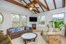 Living room featuring a ceiling fan, lofted ceiling with beams, a fireplace, and light wood-style flooring