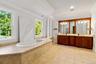 Full bathroom featuring double vanity, a tub with jets, ornamental molding, light tile patterned floors, and a chandelier