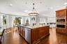 Kitchen featuring brown cabinets, ornamental molding, light stone countertops, a chandelier, and stainless steel appliances
