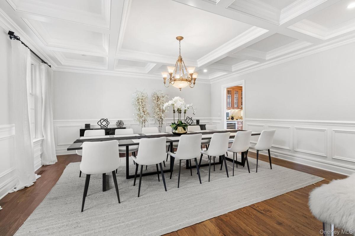 Dining area featuring beam ceiling, dark wood-style floors, a chandelier, a decorative wall, and coffered ceiling