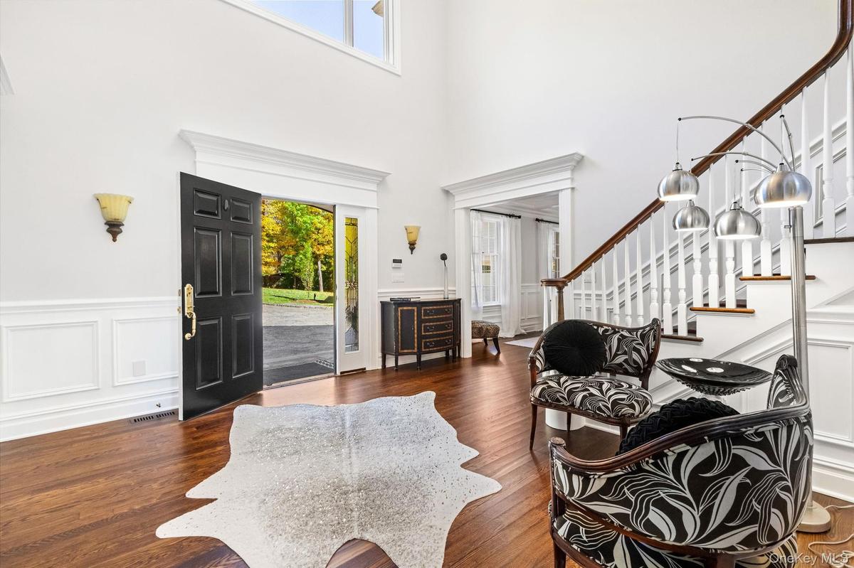 Foyer entrance with stairs, wood finished floors, a decorative wall, a towering ceiling, and a wainscoted wall