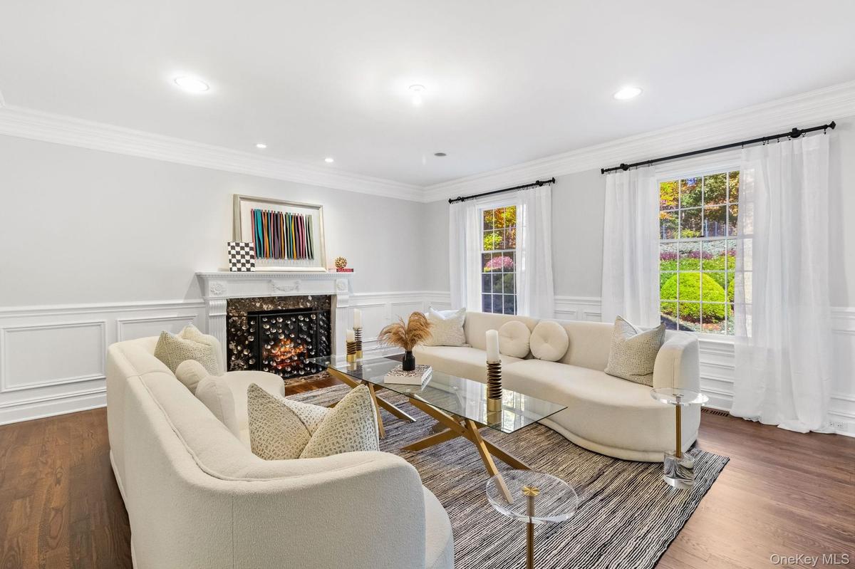 Living room featuring a high end fireplace, dark wood-style floors, ornamental molding, a decorative wall, and wainscoting