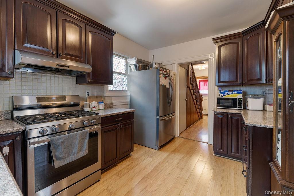 Kitchen with stainless steel appliances, dark brown cabinets, ventilation hood, light hardwood / wood-style flooring, and tasteful backsplash