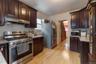 Kitchen with stainless steel appliances, dark brown cabinets, ventilation hood, light hardwood / wood-style flooring, and tasteful backsplash