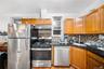 Kitchen with appliances with stainless steel finishes, brown cabinetry, under cabinet range hood, tasteful backsplash, and dark stone counters
