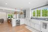 Kitchen featuring a peninsula, decorative light fixtures, white cabinetry, beverage cooler, and light stone counters