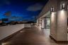 A sleek upper-level terrace illuminated by modern wall sconces, set against the dramatic glow of the evening sky. Expansive wood decking and clean arc