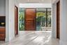 A grand modern entry framed by warm wood accents, floor-to-ceiling glass, and abundant natural light. Clean architectural lines and a dramatic pivot d