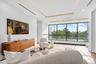 A serene waterfront bedroom showcasing clean modern lines, warm wood accents, and expansive windows framing tranquil water views. Bright and beautiful