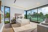 A bright and contemporary guest bedroom featuring floor-to-ceiling glass and direct access to a private balcony overlooking lush greenery. Airy and re