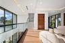 A striking upper-level gallery hallway featuring warm wood floors, sleek glass railings, and expansive windows that flood the space with natural light