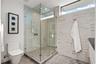 A bright, modern bath showcasing a glass-enclosed walk-in shower, sleek fixtures, and crisp neutral stone finishes. Clean-lined and thoughtfully appoi