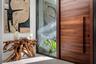 A sophisticated entry detail featuring a striking wood pivot door, sleek glass panels, and curated contemporary art that creates an immediate design s