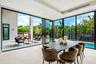 A light-filled dining area wrapped in floor-to-ceiling glass, offering seamless views of the lush garden and pool beyond. Modern and inviting, this el