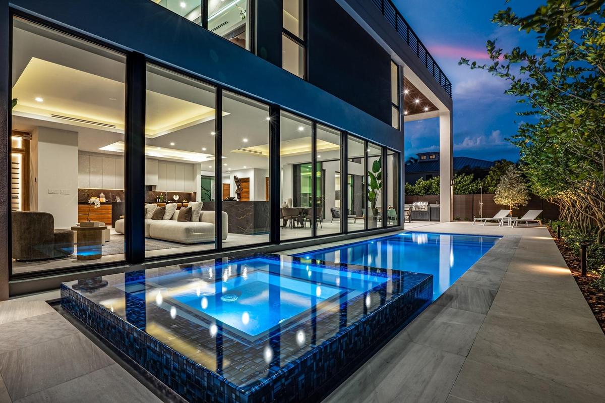 A dramatic evening poolscape framed by floor-to-ceiling glass walls that dissolve the boundary between indoors and out. Sleek, modern, and illuminated
