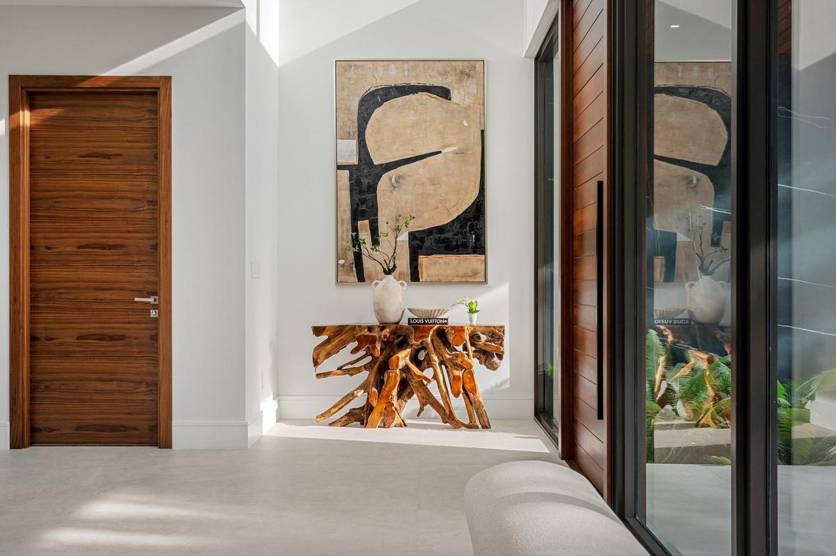 A refined entry vignette showcasing a rich wood front door, sleek glass panels, and curated modern artwork that sets an elegant first impression. Clea