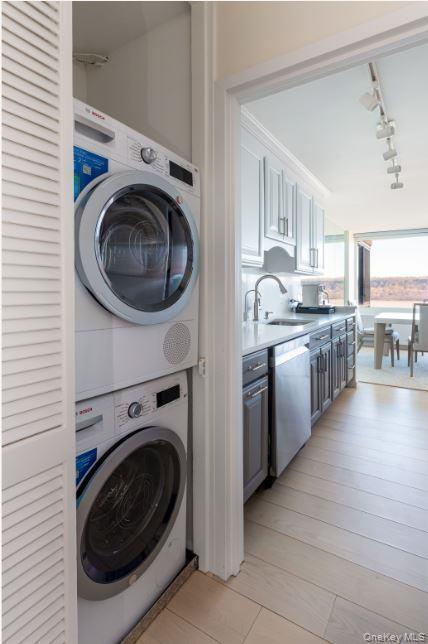 Laundry area with stacked washing maching and dryer, laundry area, a sink, and rail lighting