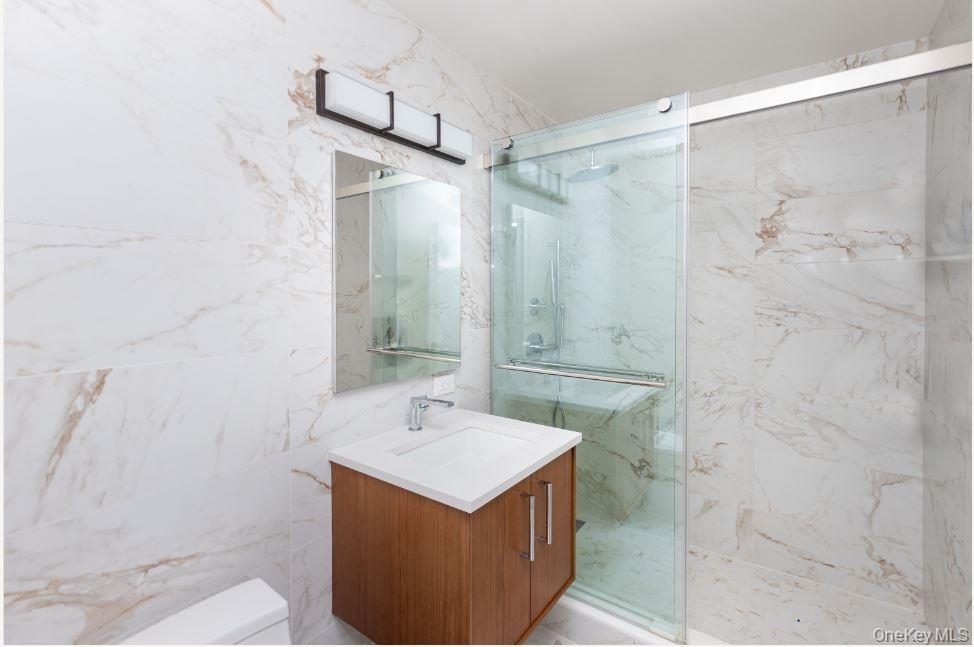 Bathroom featuring a marble finish shower, tile walls, toilet, and vanity
