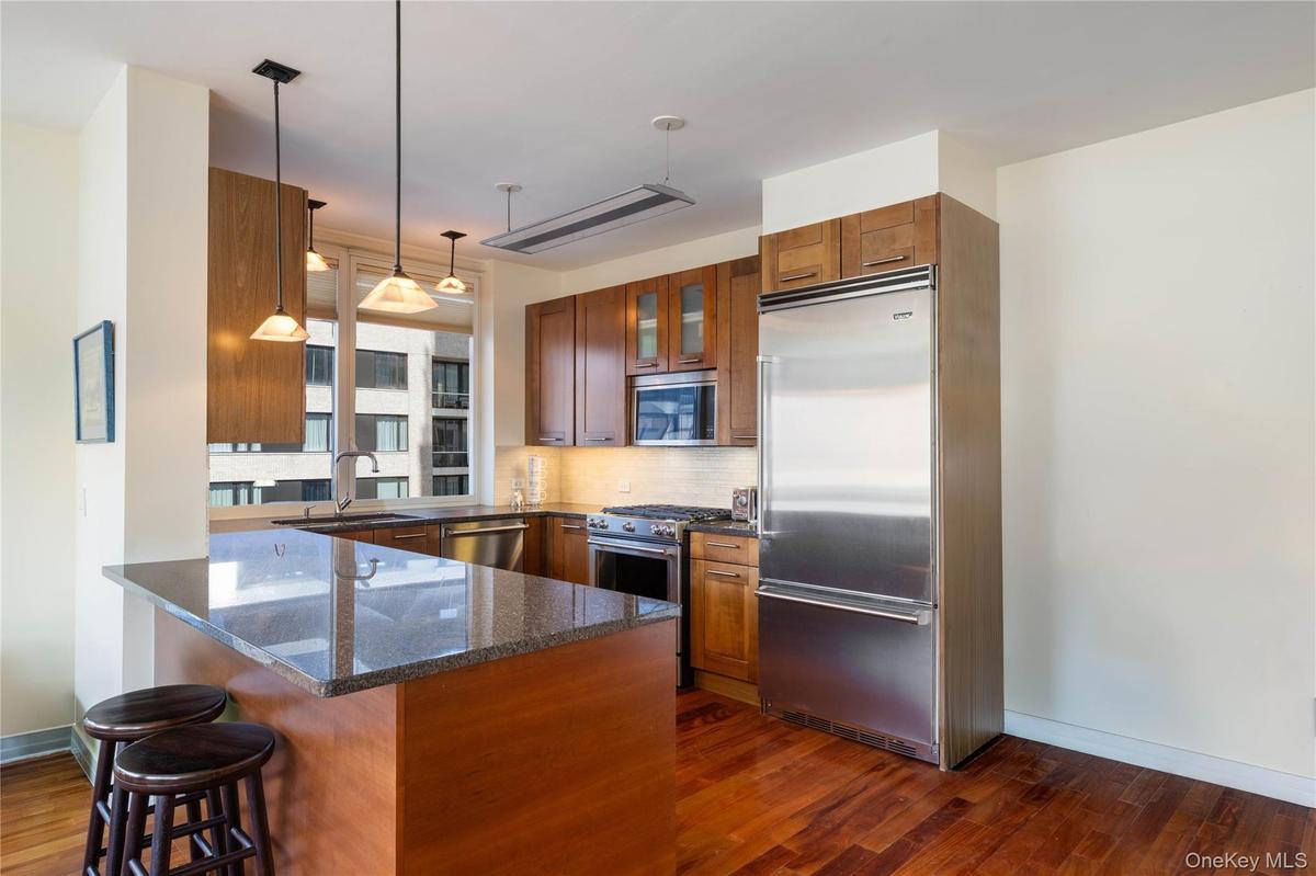 Kitchen with dark stone counters, high end appliances, backsplash, wood finish cabinetry, and decorative light fixtures