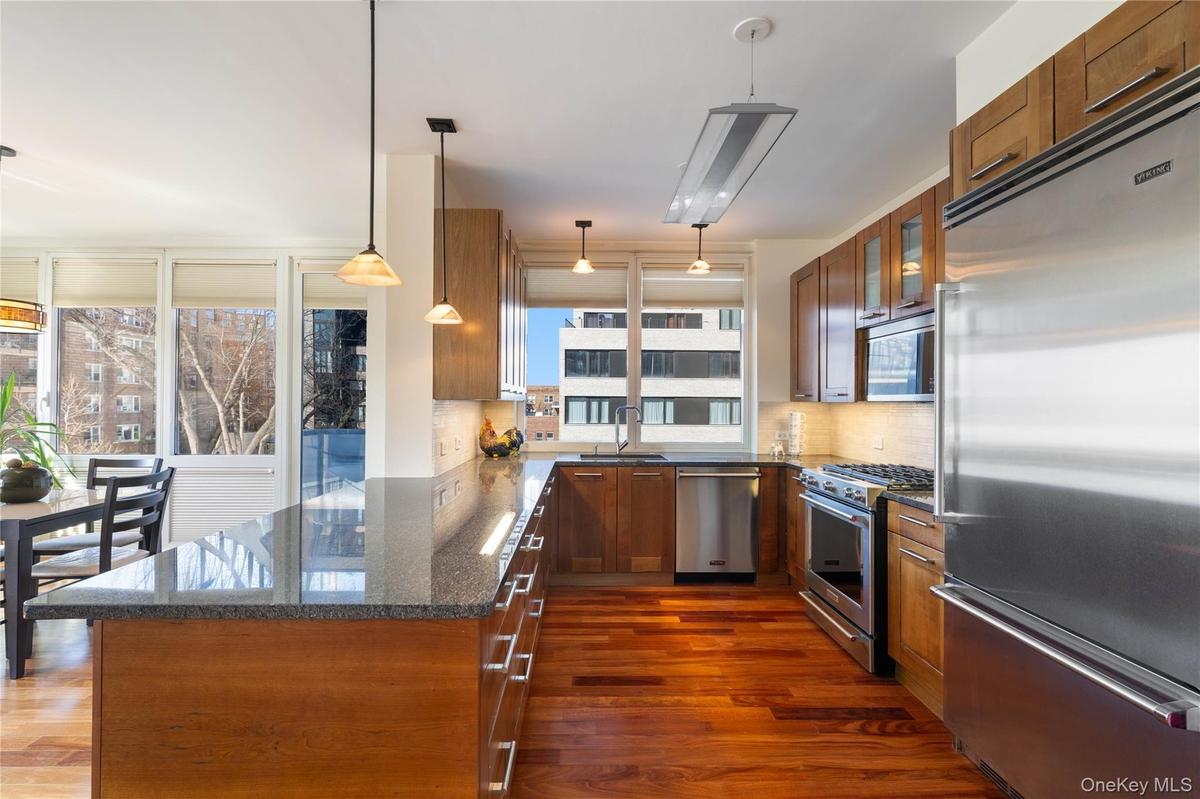 Kitchen with high end appliances, dark stone countertops, wood finish cabinets, and a peninsula