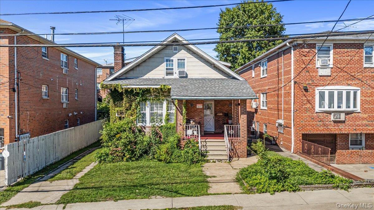 Bungalow-style house featuring roof with shingles, covered porch, a chimney, brick siding, and a front yard