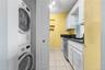 Stackable washer and dryer unit, white cabinetry, black countertops, stainless steel dishwasher, and tile flooring