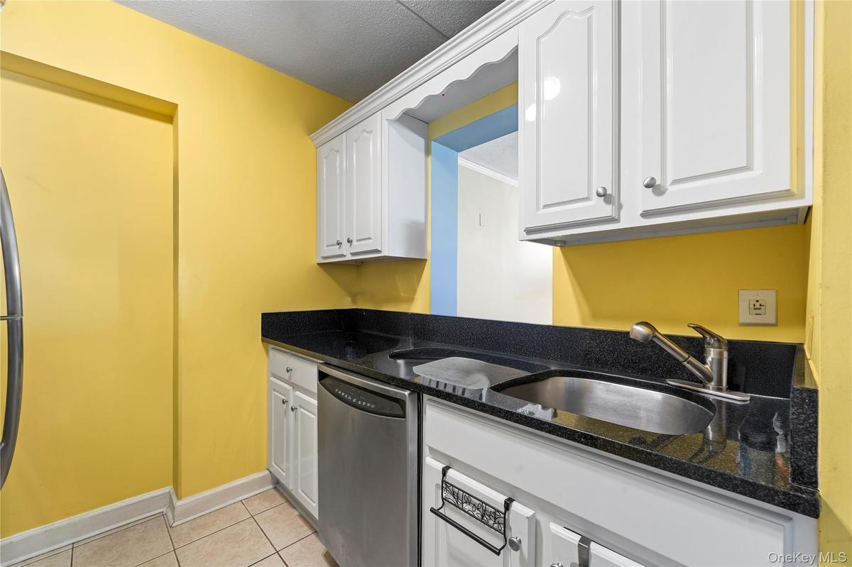 Kitchen featuring white cabinetry, dark countertops, a stainless steel dishwasher, and a stainless steel sink with a pull-out faucet
