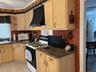 Kitchen featuring range with gas cooktop, ventilation hood, white microwave, light brown cabinetry, and open shelves