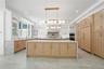Kitchen with light brown cabinetry, glass insert cabinets, a raised ceiling, light stone countertops, and recessed lighting