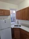 Kitchen with freestanding refrigerator, brown cabinetry, and light stone countertops