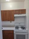 Kitchen featuring white gas range oven, brown cabinetry, under cabinet range hood, and light stone countertops
