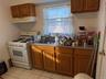 Kitchen featuring brown cabinetry, white gas range, under cabinet range hood, light tile patterned flooring, and dark countertops