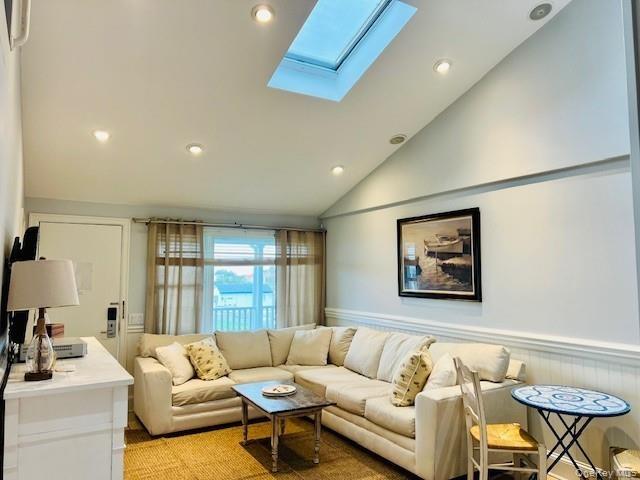 Living room featuring vaulted ceiling, recessed lighting, a skylight, and a wainscoted wall
