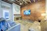 Tiled living area with beam ceiling, a glass covered fireplace, brick wall, and a high ceiling