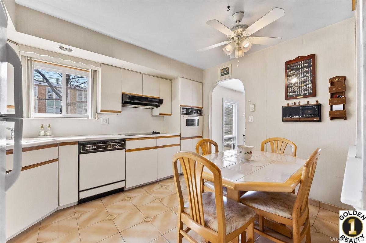 Kitchen with light countertops, white appliances, arched walkways, ceiling fan, and two tone cabinets