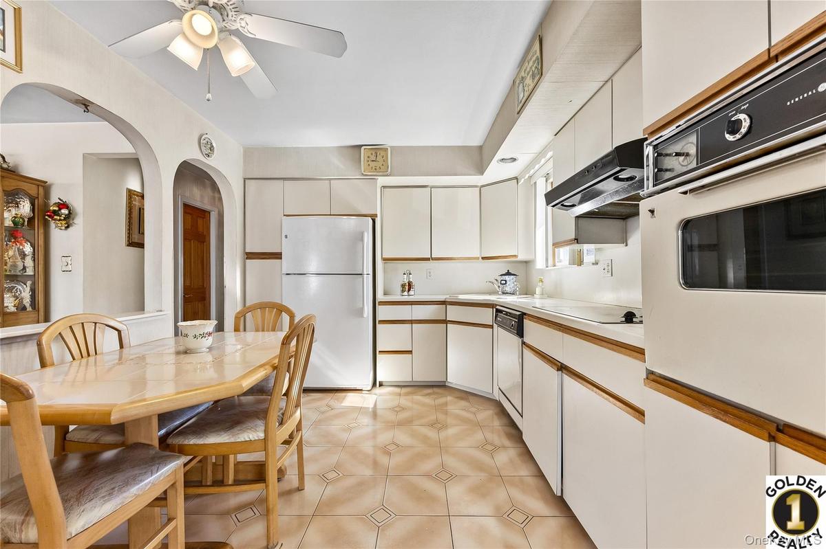 Kitchen featuring white appliances, light countertops, two tone cabinetry, a ceiling fan, and arched walkways