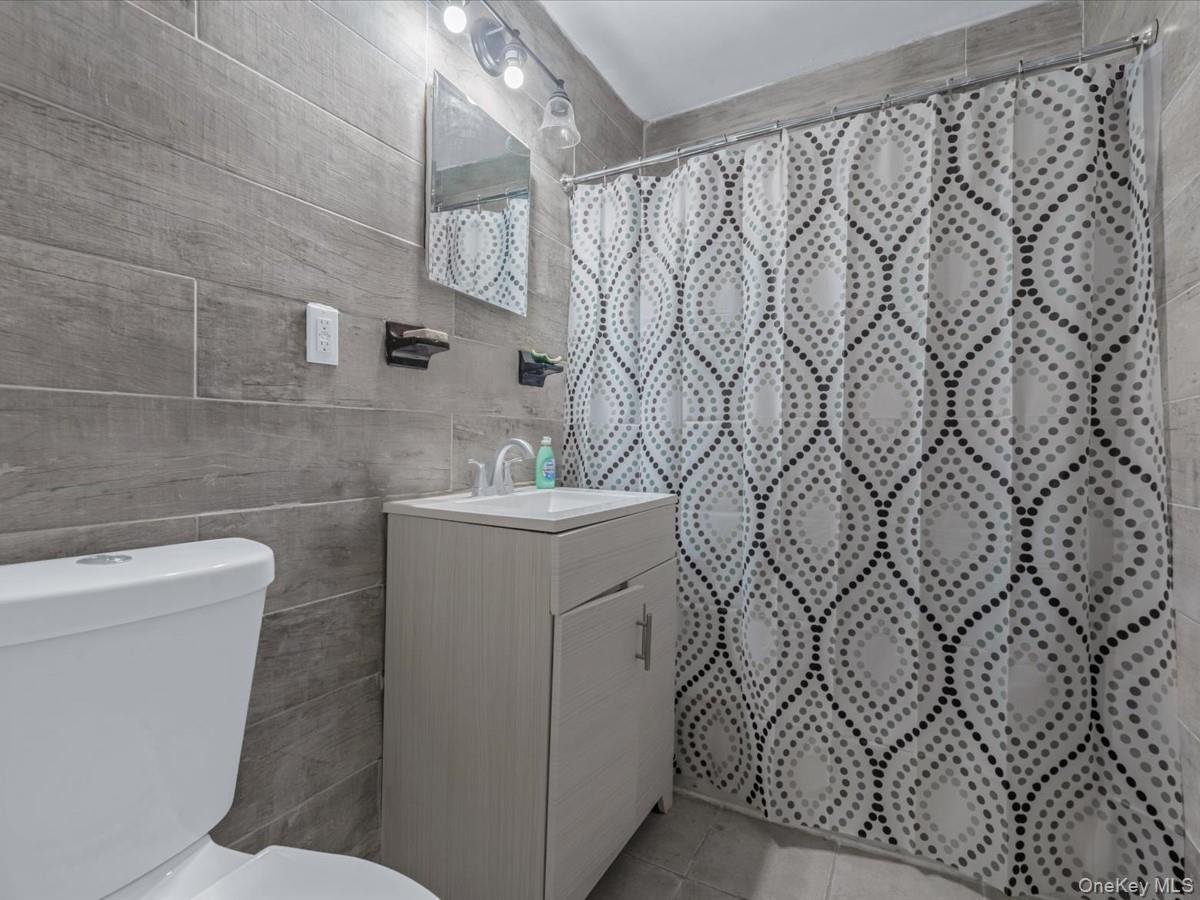 Bathroom with vanity, a shower with shower curtain, light tile patterned floors, and tile walls